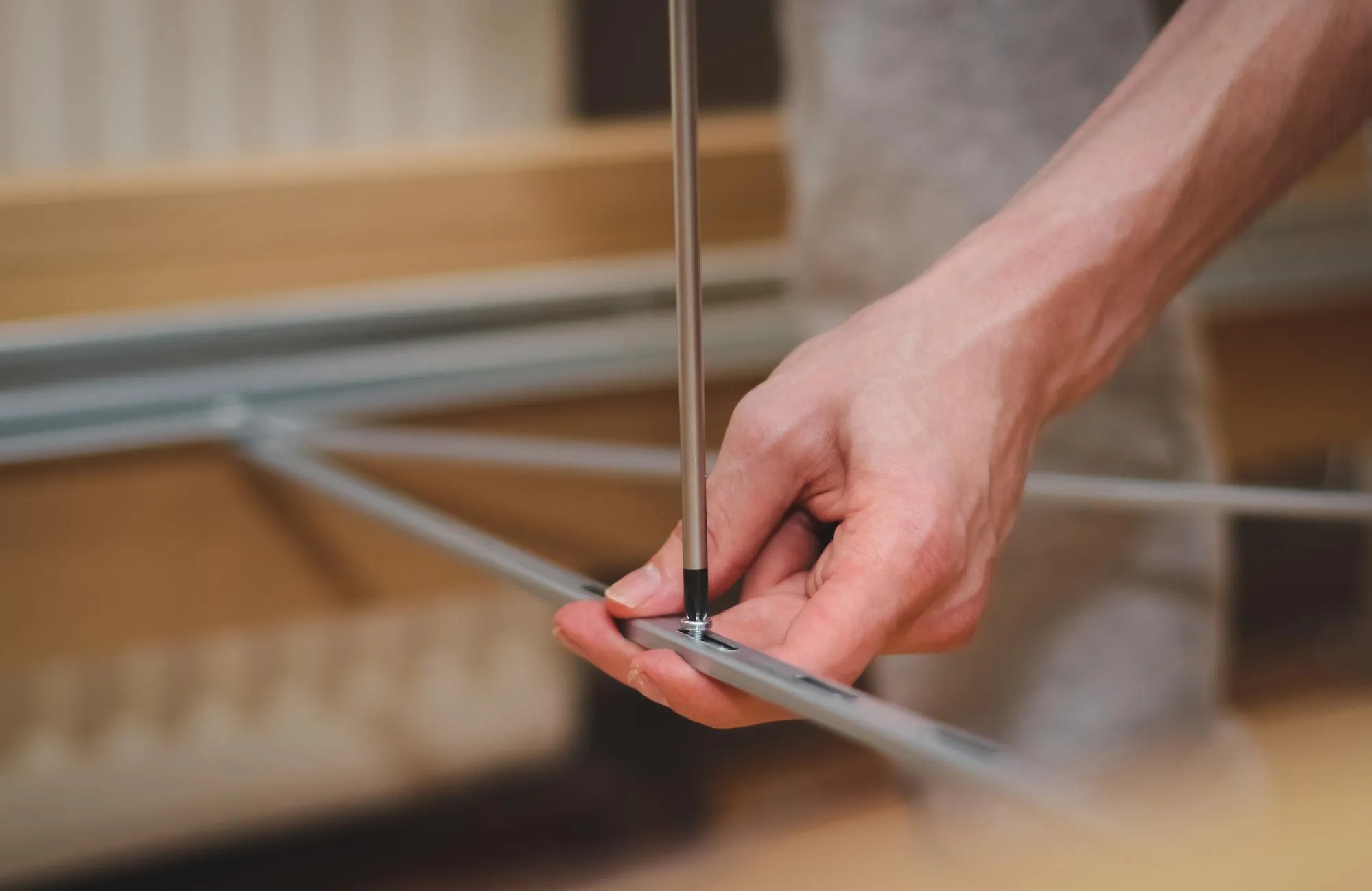 The hands of a caucasian young man are twisting a screw with a screwdriver connecting a metal part to a bed