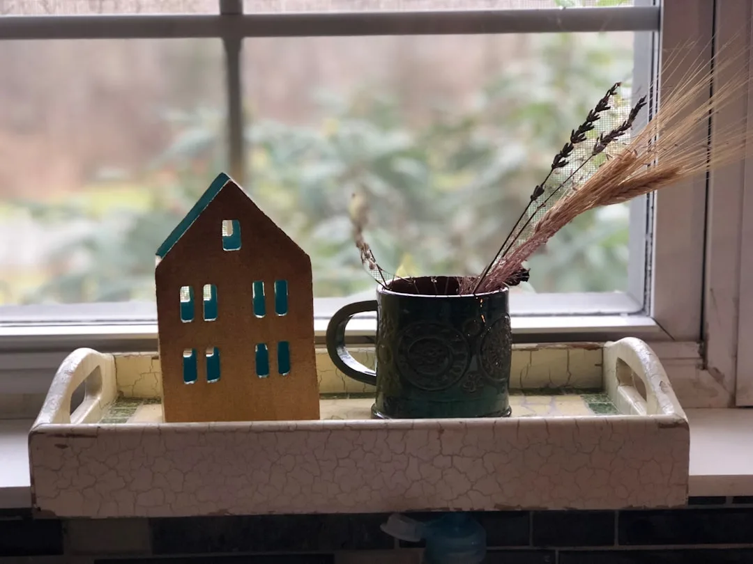 wheat in black mug beside house scale model near window