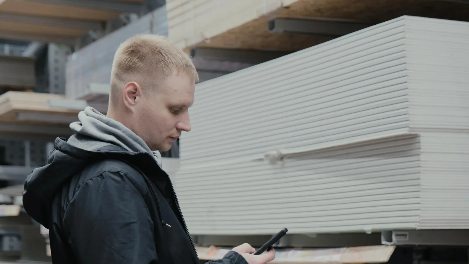 A man in a hardware store chooses wooden sheets of osb The buyer in the store chooses chipboard Buying plywood at a hardware store Blockboards in a hardware store