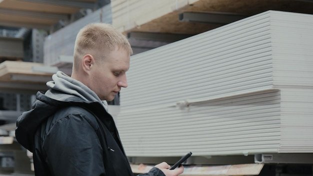 A man in a hardware store chooses wooden sheets of osb The buyer in the store chooses chipboard Buying plywood at a hardware store Blockboards in a hardware store