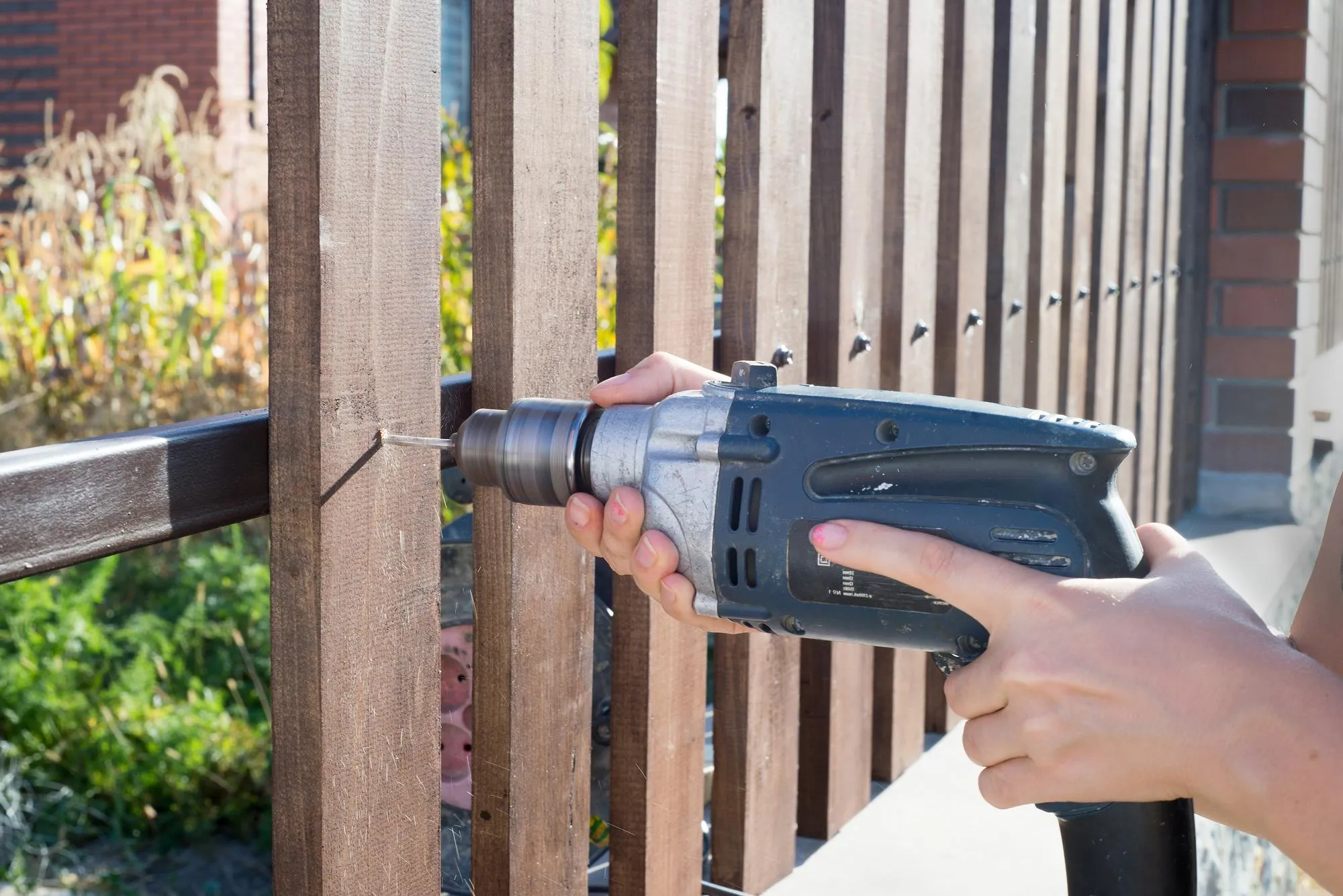 Woman hands drilling wood plank fence to metal construction Building a wooden fence with a drill and screw