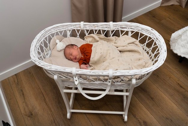 A Caucasian newborn baby sleeps in a Moses basket with a stand in the bedroom