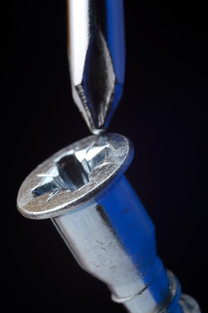 Chrome screwdriver twists or unscrews the yellow self-tapping screw. close-up.