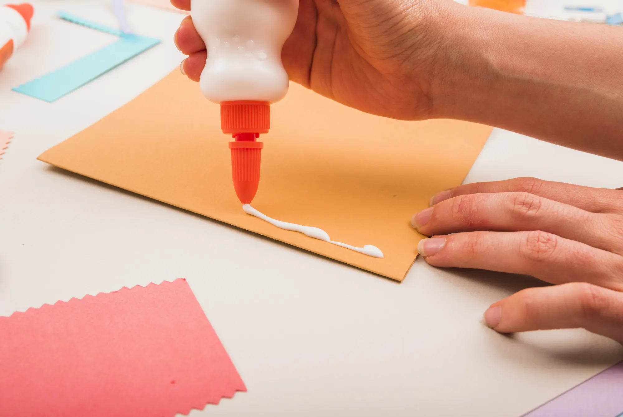 Close-up of a person's hand applying white glue on paper
