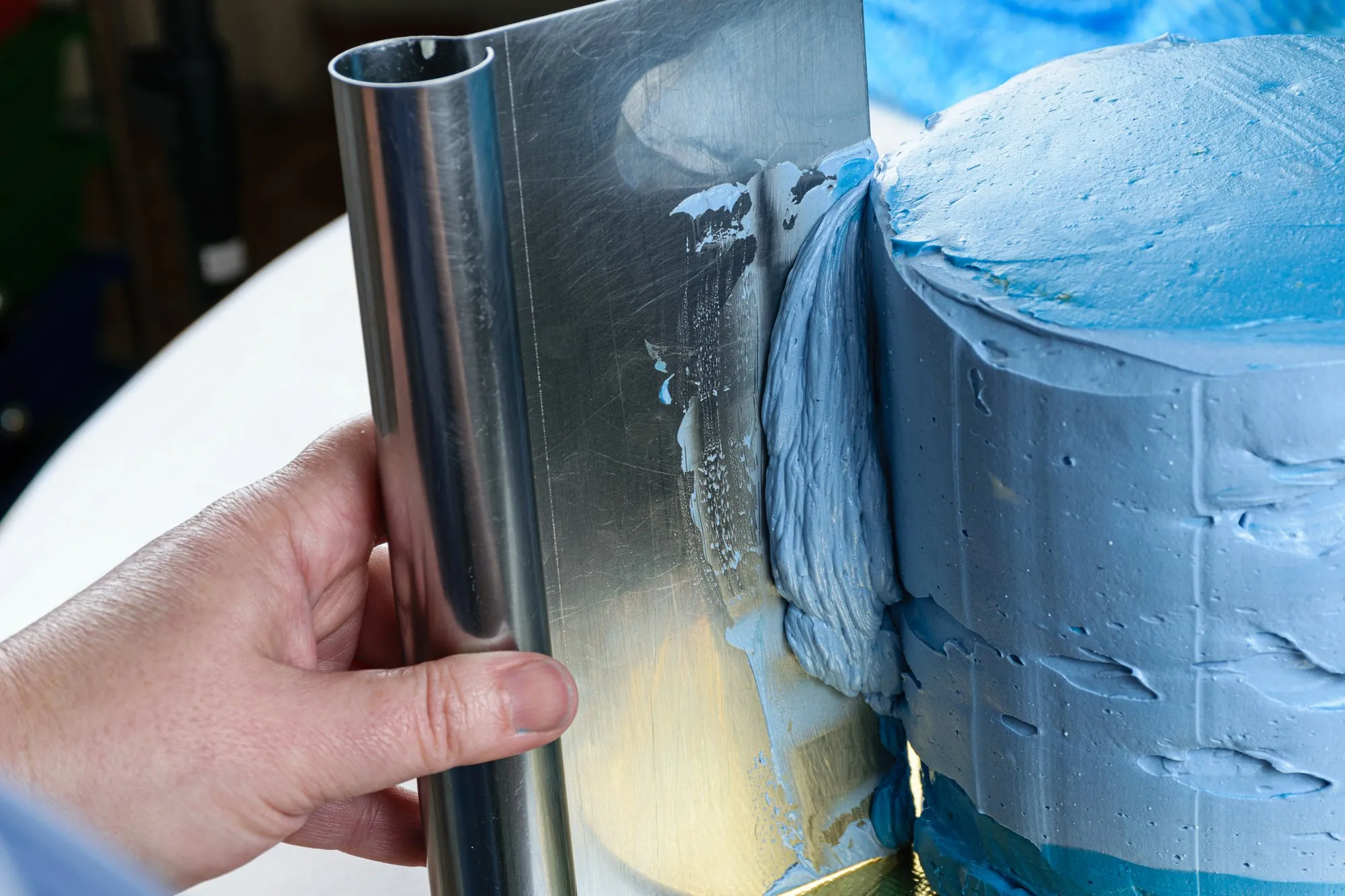 Closeup of a confectioner using a spatula on the side of the cake to spread the frosting.