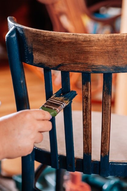 Closeup of hand painting aged chair in blue color with brush in workshop for furniture renovation Reuse of old things Thinking about future through sustainable actions