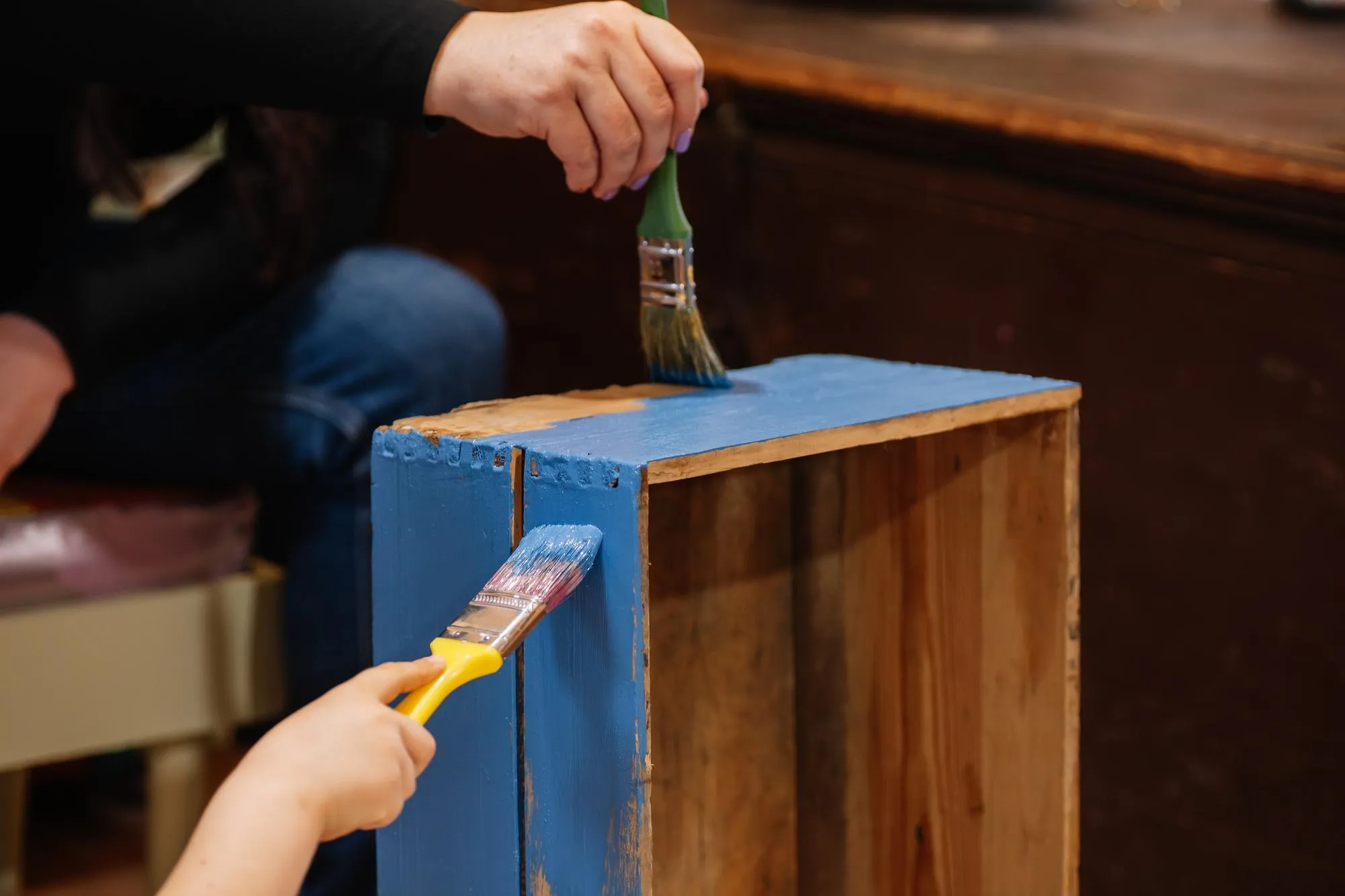 Closeup of young girl and woman hands with brushes slowly painting very old wooden closet drawer in blue color Reuse of old things Sustainable ecofriendly actions for planet future