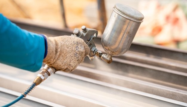 Construction worker painting metal structure surface coating with a spray gun at construction site