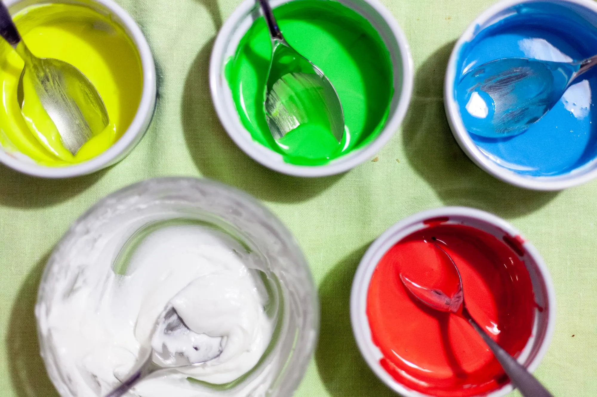 Edible colors yellow green blue white red in five bowls in a kitchen with spoons