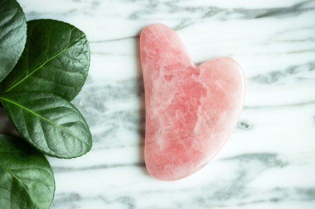 A gua sha for the face and a flower against the marble background view from above