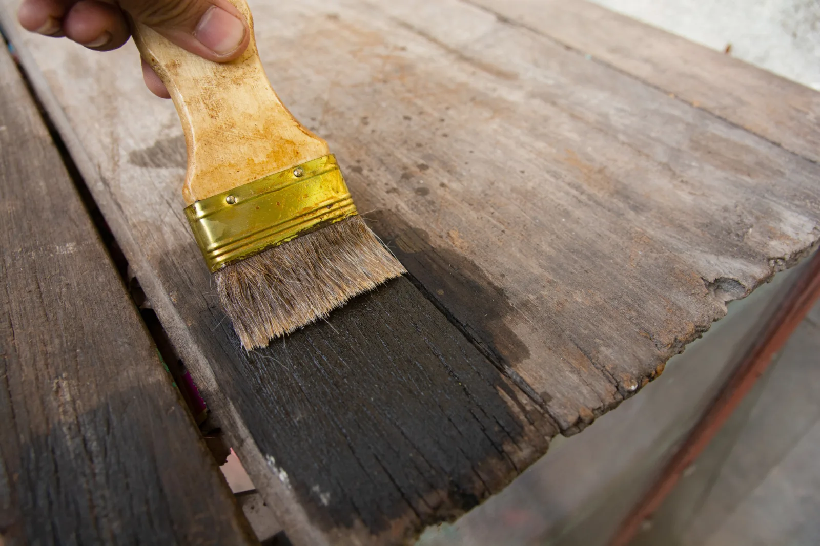 Hand holding a brush Painting wooden timber boards surface with Wood Stain
