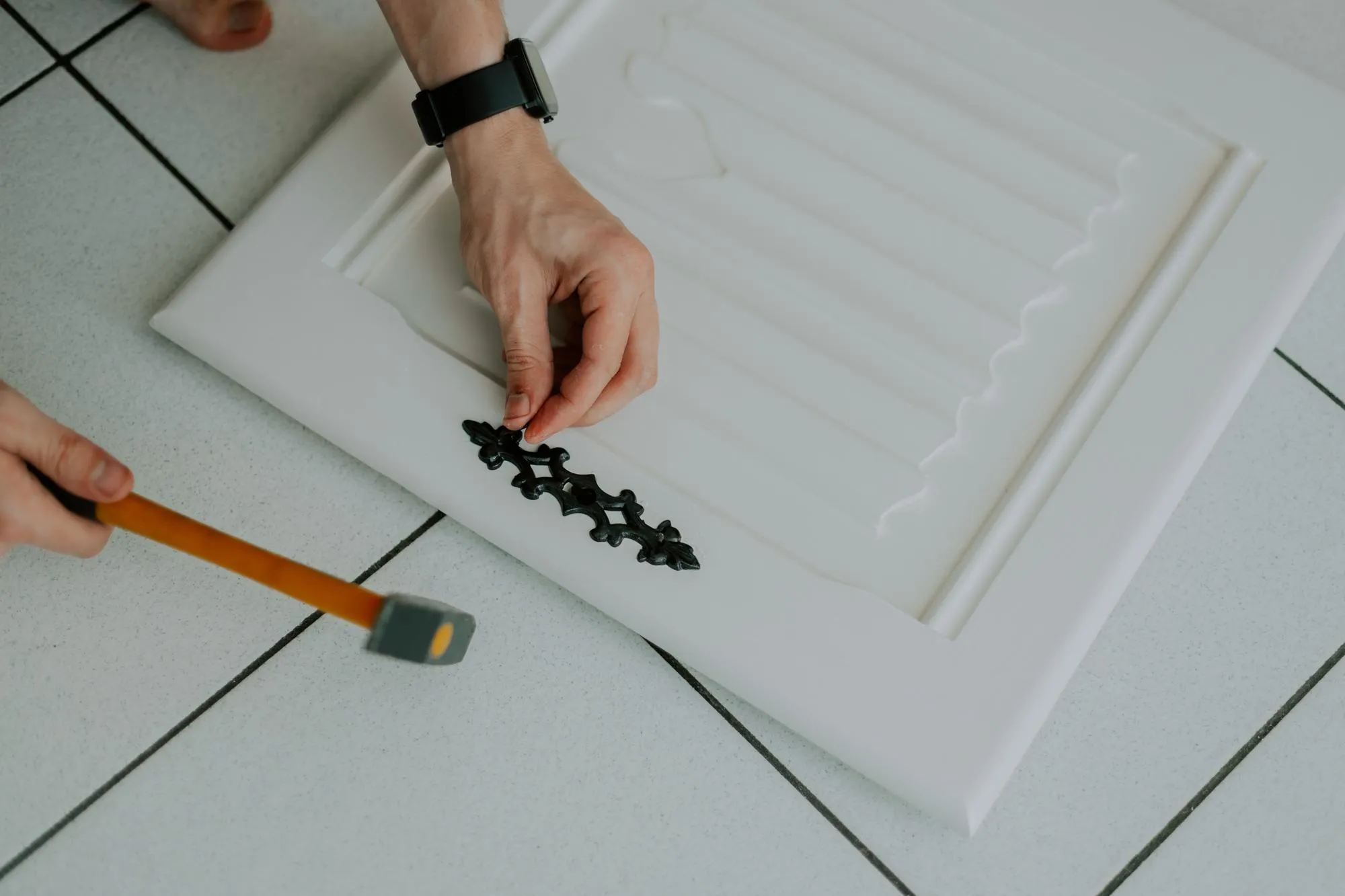 The hands of a young Caucasian man hammers a nail installing an antique carved black lock on a door