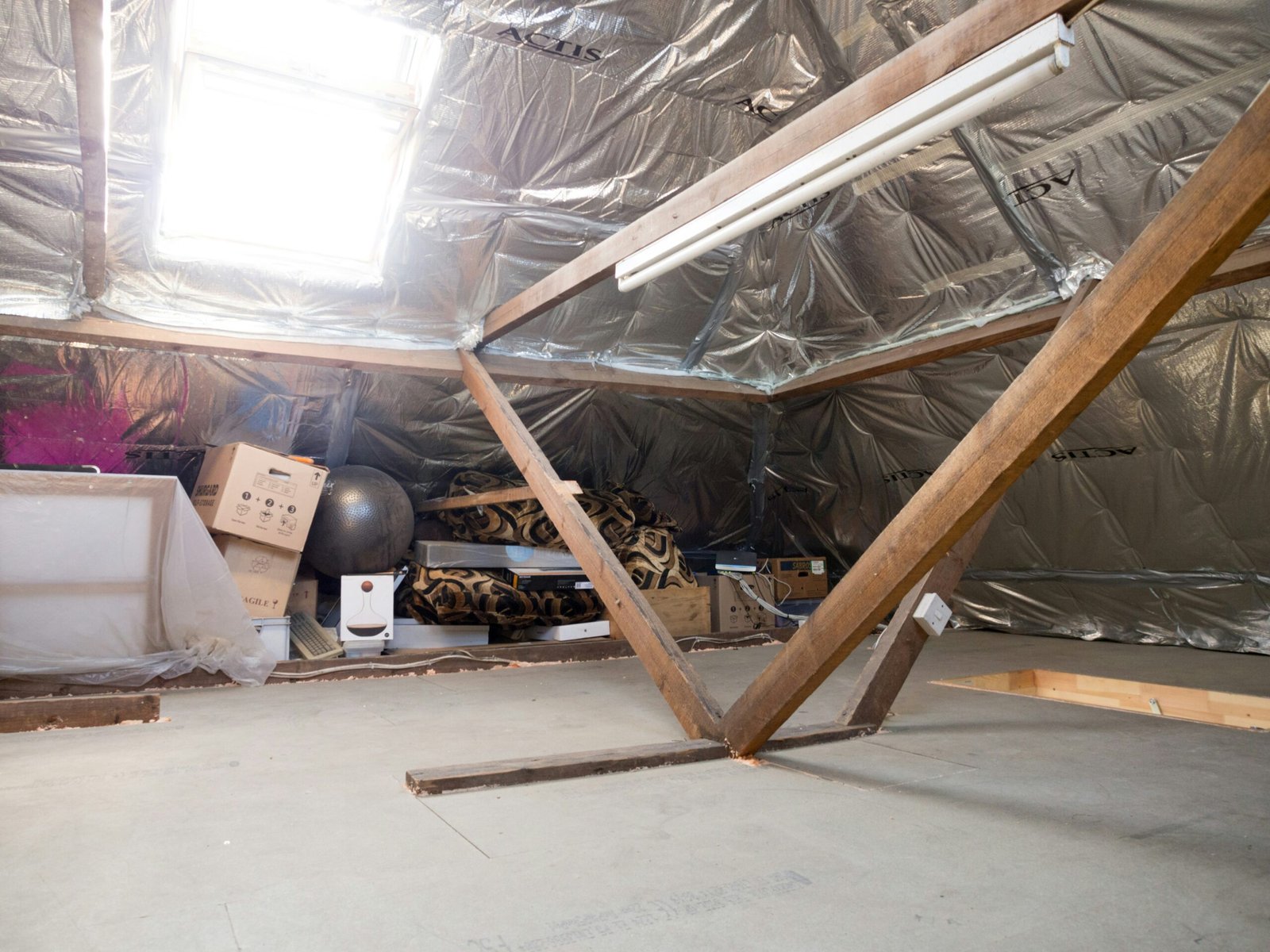 A dusty attic with insulation and wooden beams.