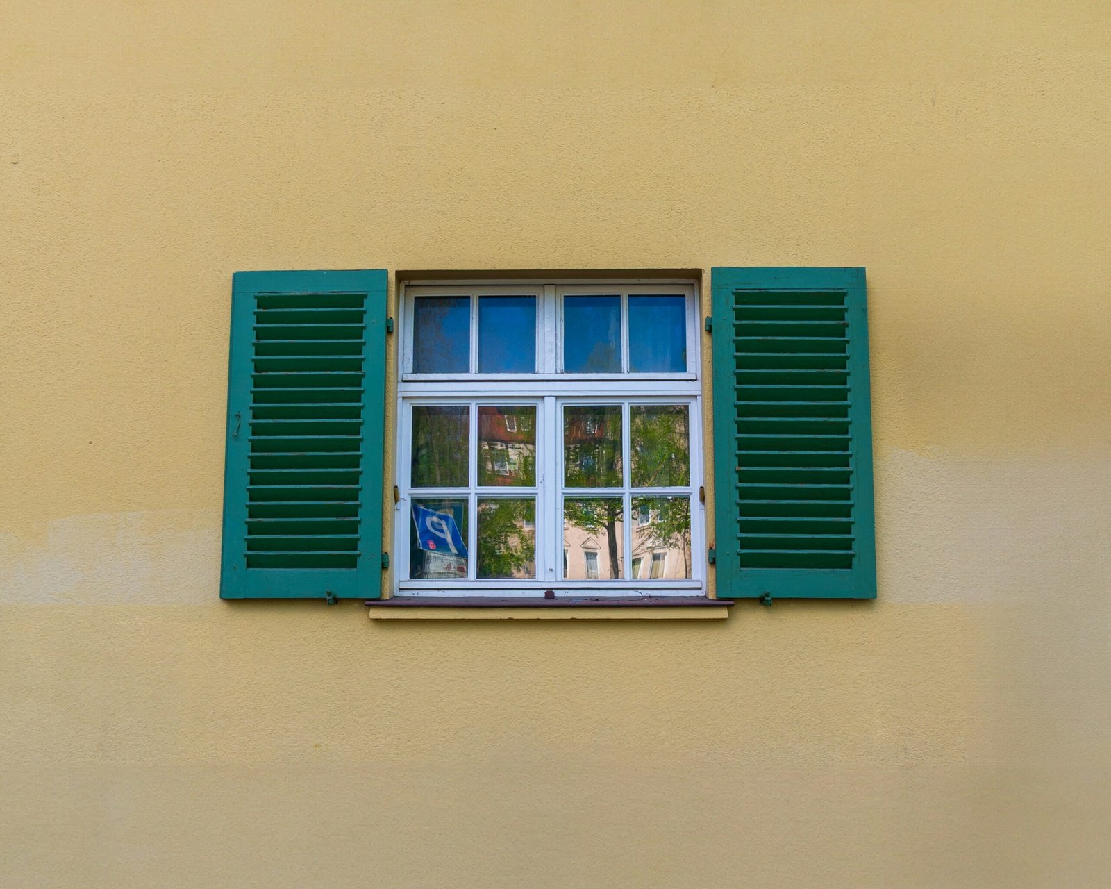 Window with green shutters against a yellow wall.