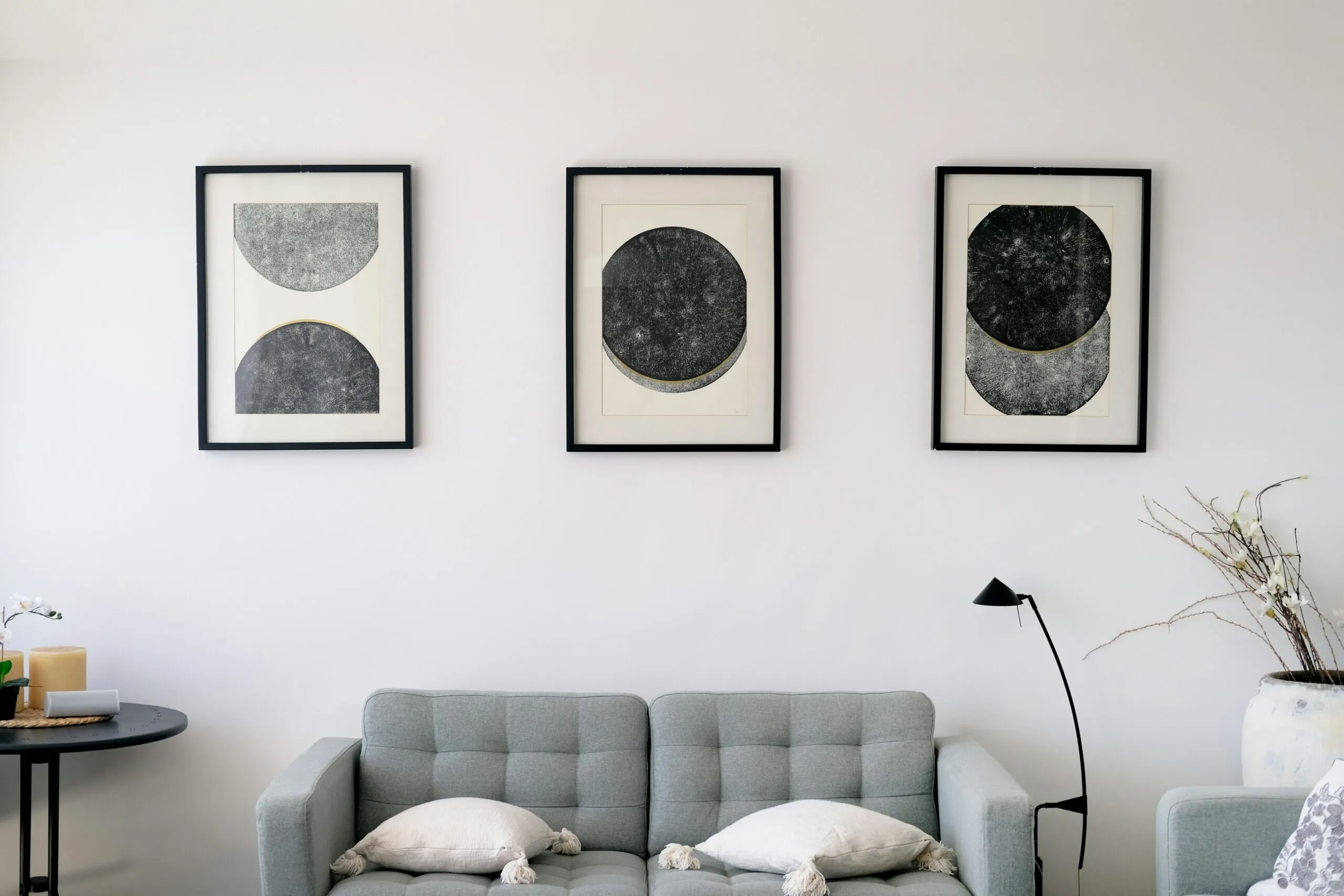 Three abstract art pieces hang above a gray sofa.
