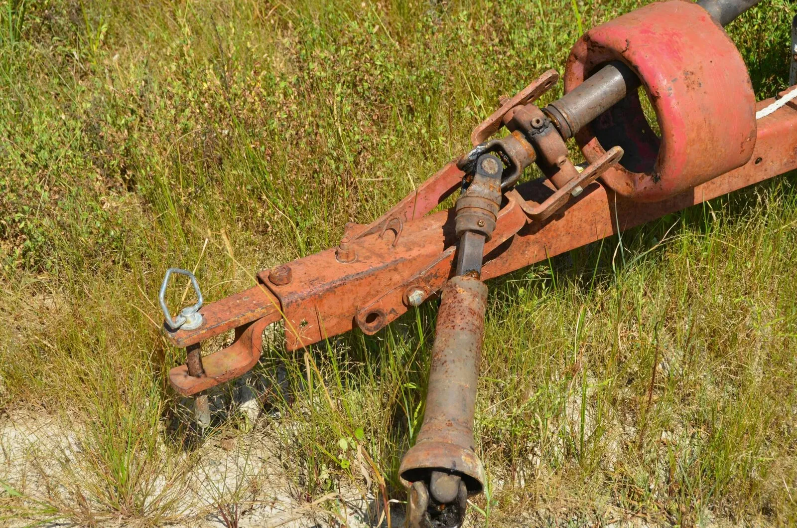 Rusty farm equipment hitch in grassy field.