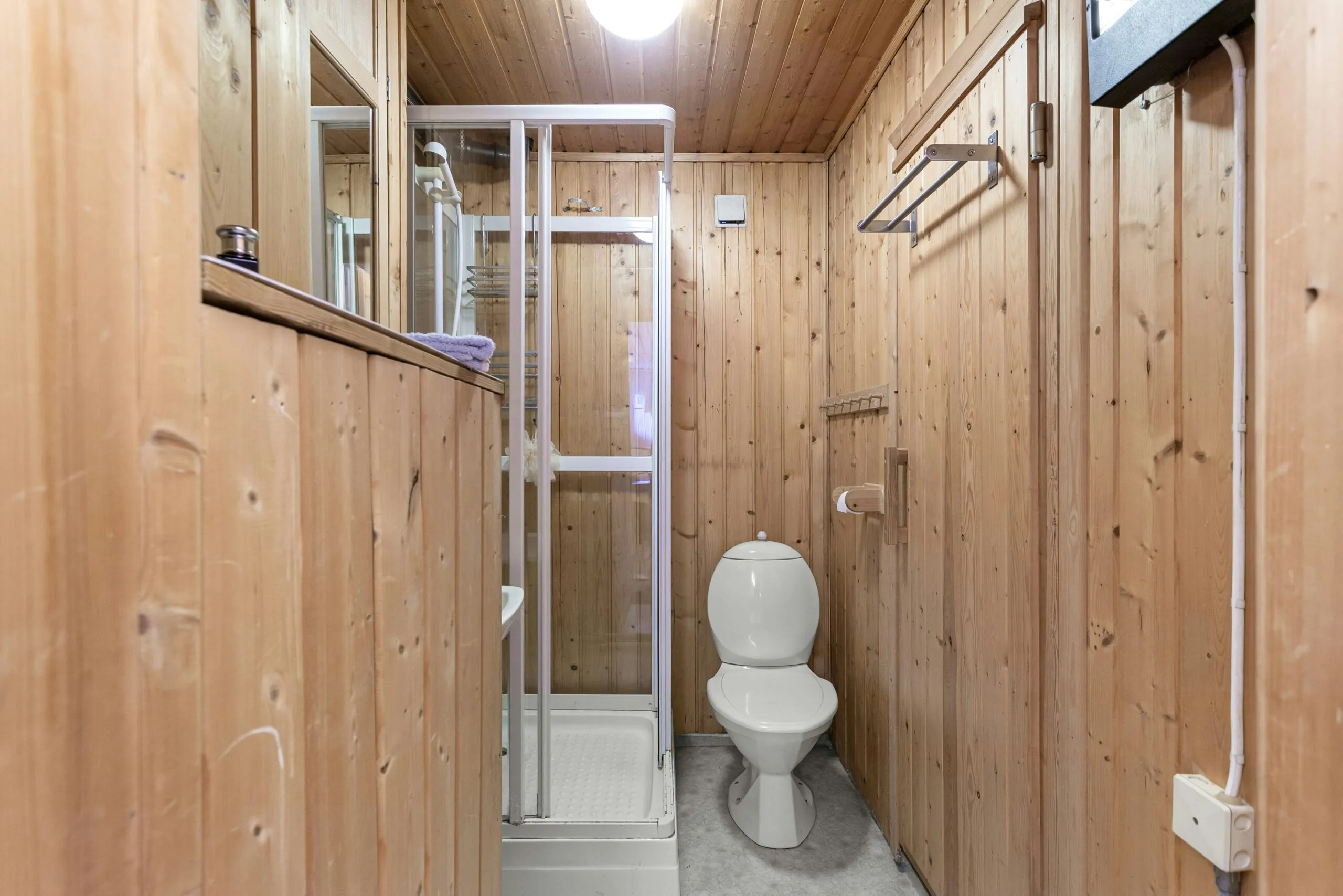 A narrow bathroom with wooden walls and a white toilet