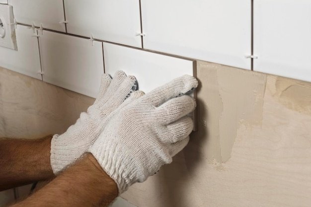 Male Worker Master Laying Ceramic Tiles on the Wall of Kitchen Repairman Placing White Modern Tiles Spreading Adhesive Builder Installing Tile at Repair Renovation Work Professional Tiling 4K