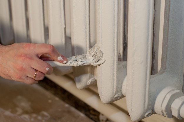 A man's hand with a ring paints the battery with a white paint brush