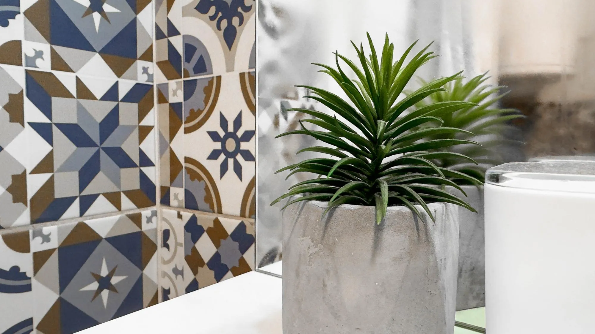 Minimalist Bathroom Decor with Concrete Planter and Patterned Ceramic Tiles A stylish and modern setup featuring a green plant in a concrete pot alongside intricate geometric tile patterns