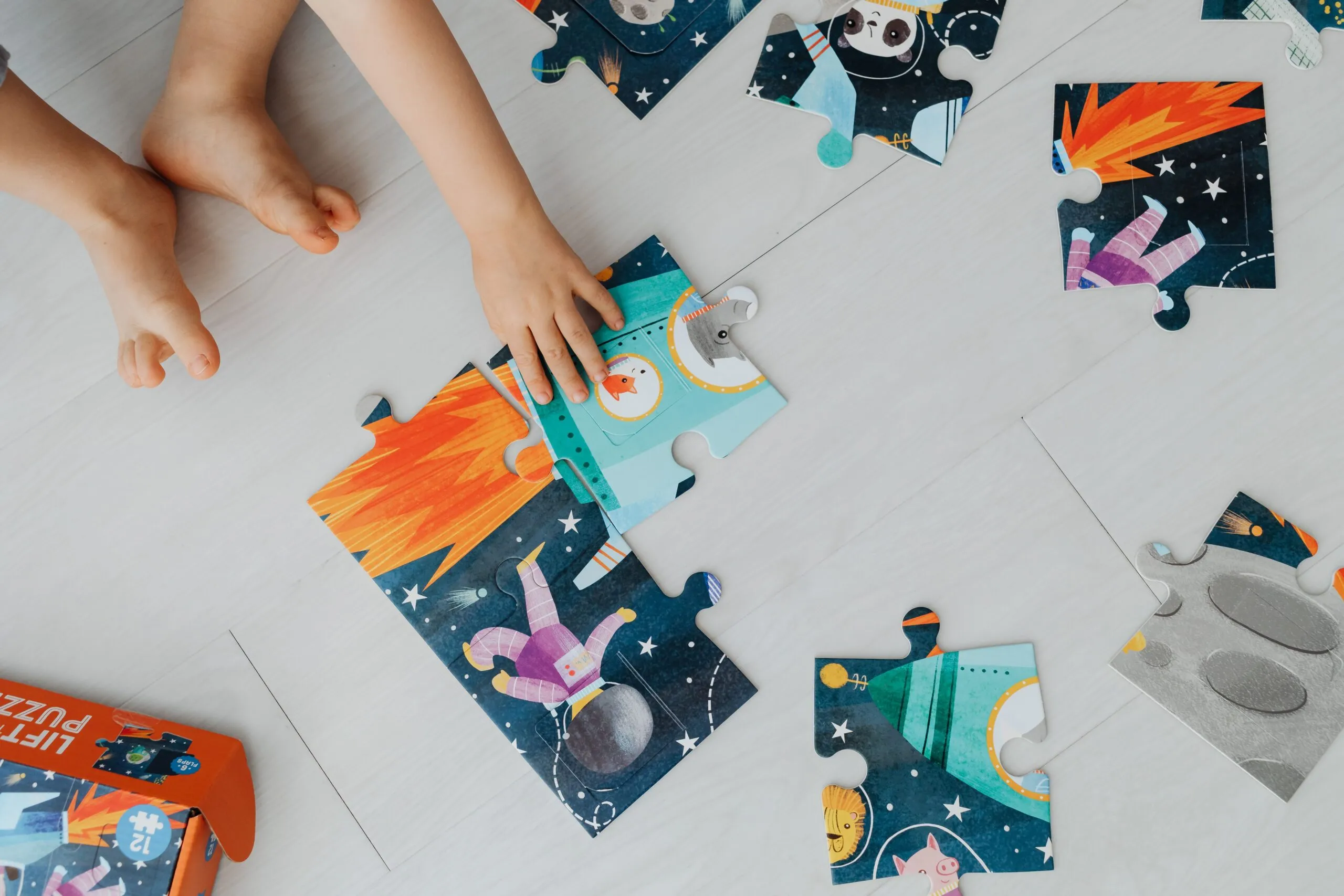 Top view of child assembling space-themed puzzle pieces on a light floor.