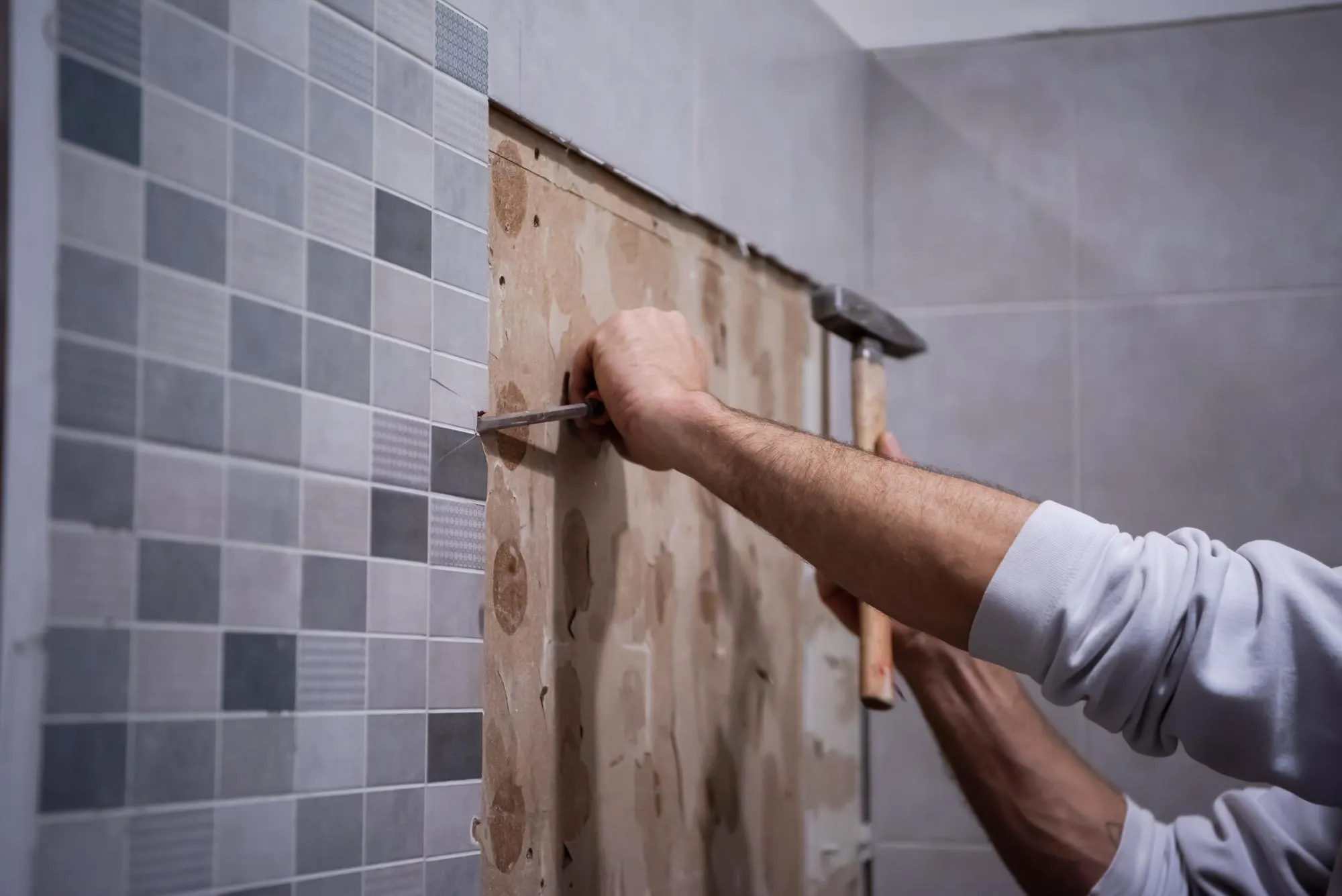 professional worker remove demolish old tiles in a bathroom with hammer and chisel