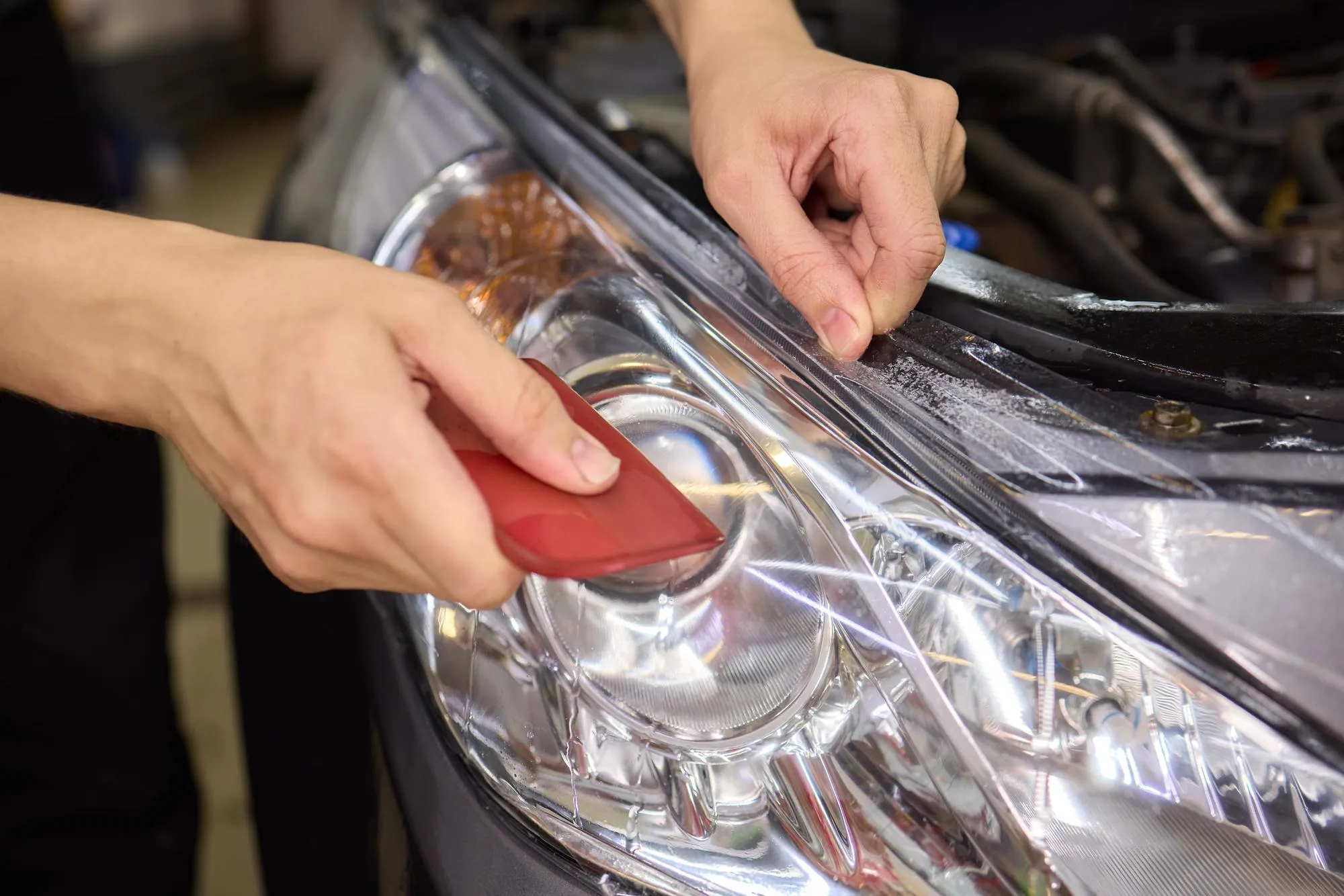 Protective film applied to car bumper in detailing workshop for safety and maintenance