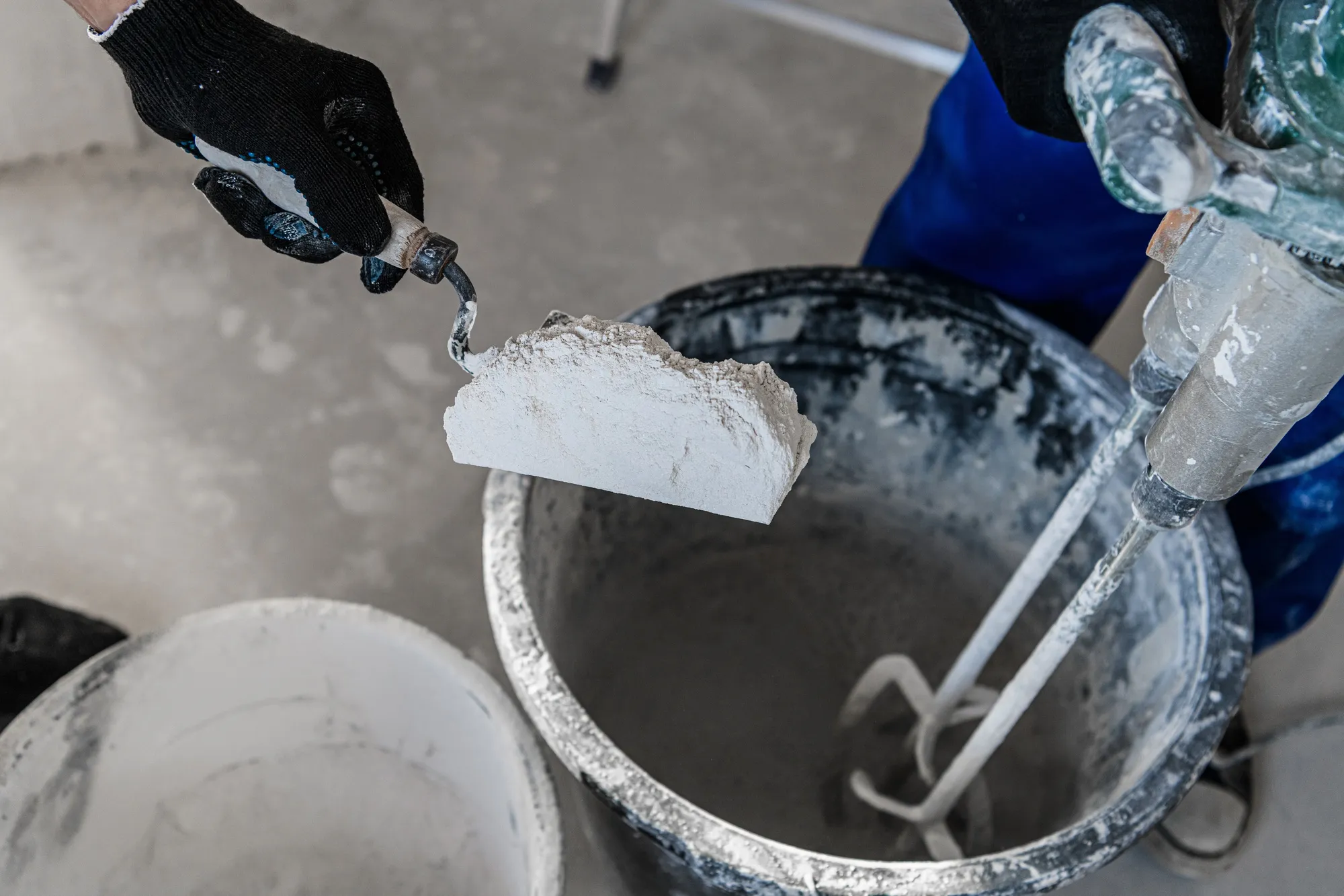 Repairer puts dry plaster into the bucket. He uses a trowel