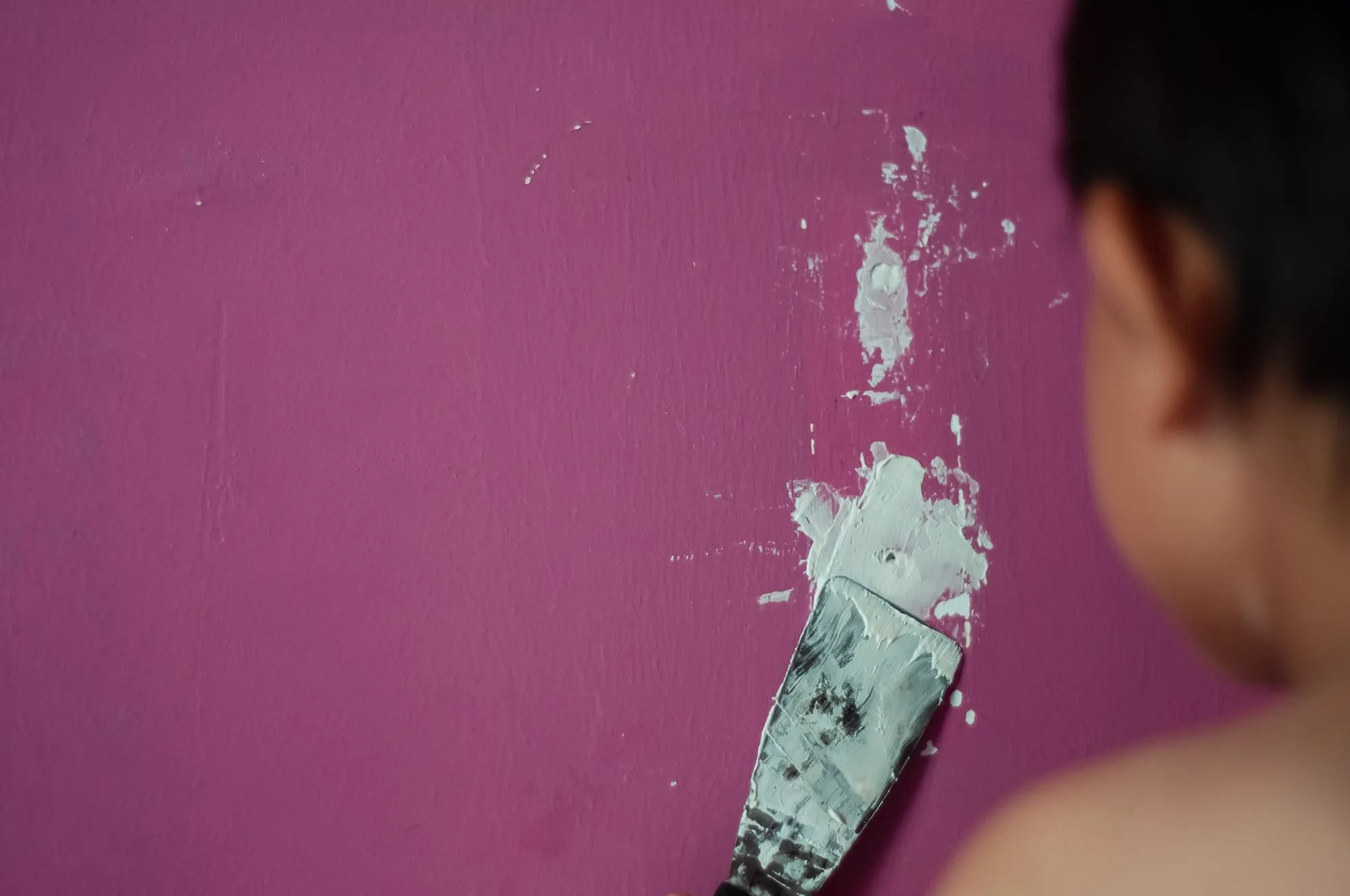 Shirtless boy filling hole with putty knife on wall