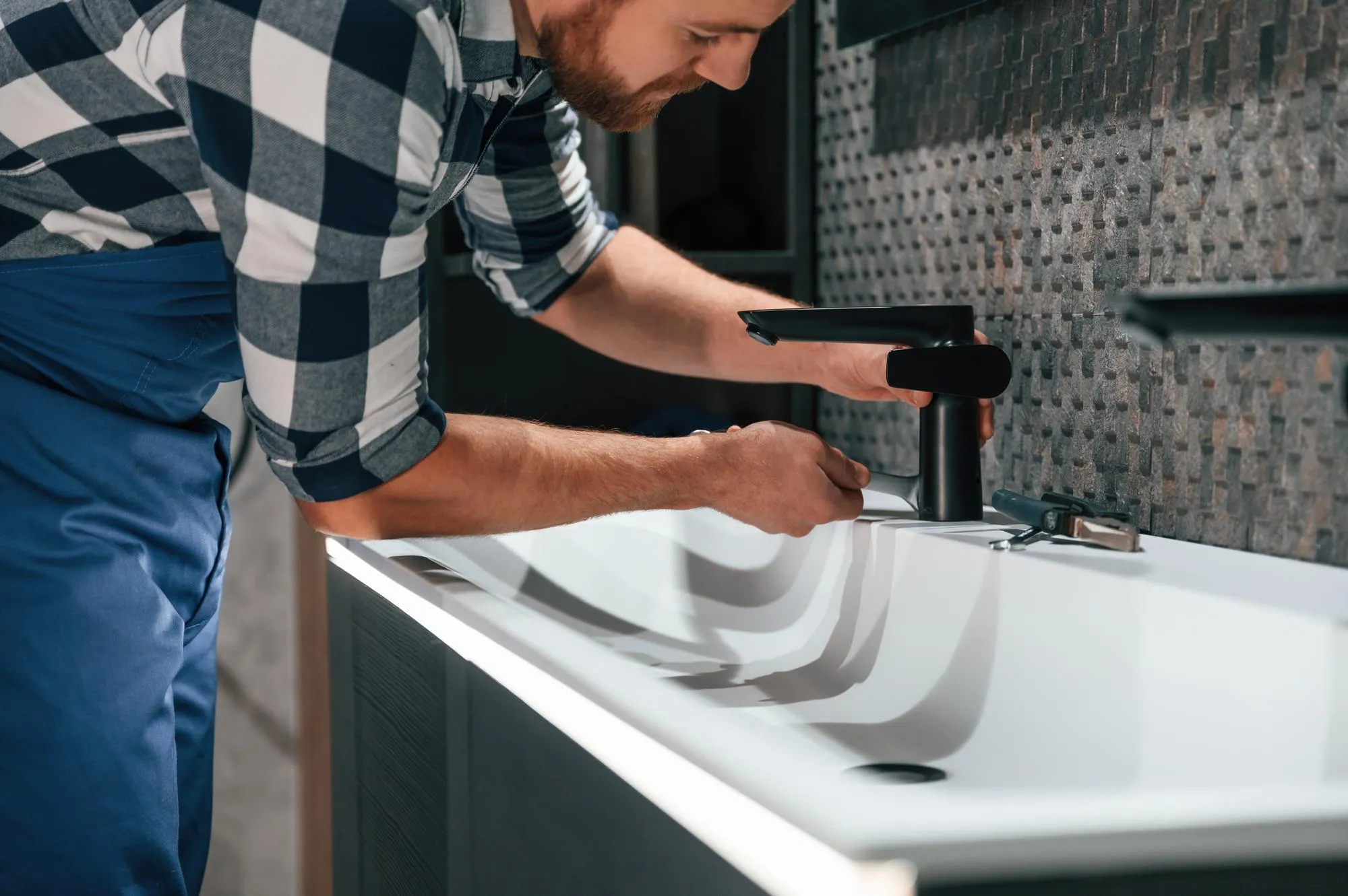 Side view Fixing water tap Plumber in blue uniform is at work in the bathroom
