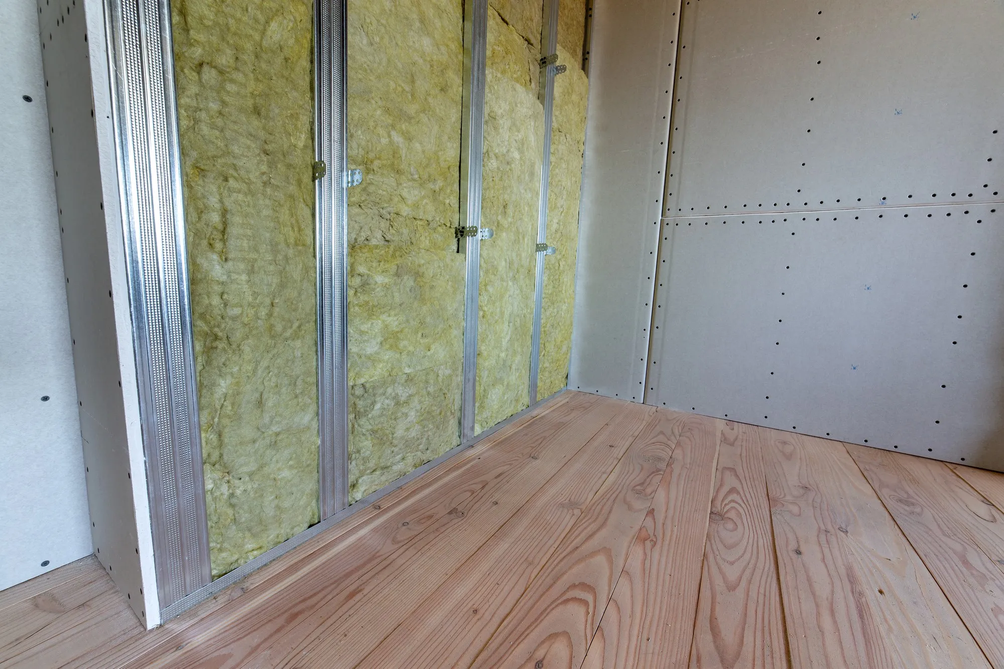 Wall of a room under renovation with mineral rock wool insulation and metal frame prepared for drywall plates.