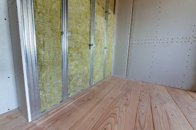 Wall of a room under renovation with mineral rock wool insulation and metal frame prepared for drywall plates.