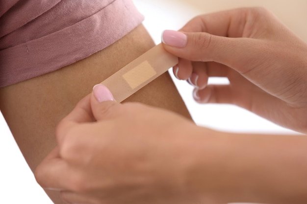Woman applying adhesive bandage on man's arm against light background closeup