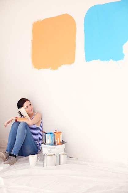 Woman choosing paint colour from swatch for new home sitting on wooden floor Woman in the house