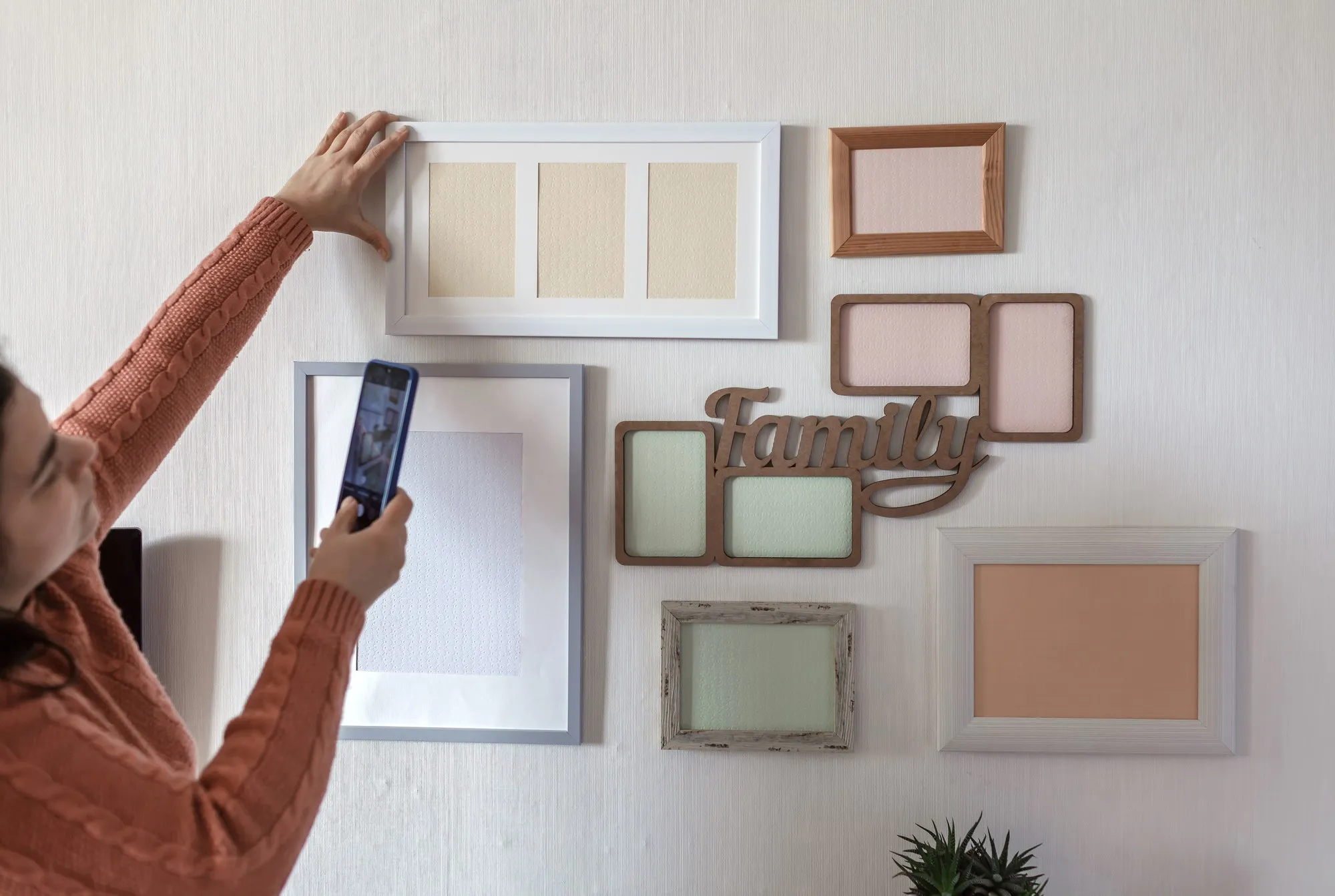Woman making photo of white wall with set of different empty vertical and horizontal picture frames, family photo gallery project to capture moment, mockup template on the white wall, lifestyle