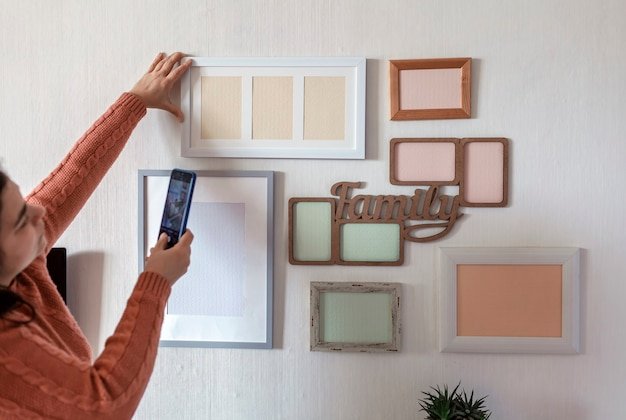 Woman making photo of white wall with set of different empty vertical and horizontal picture frames, family photo gallery project to capture moment, mockup template on the white wall, lifestyle