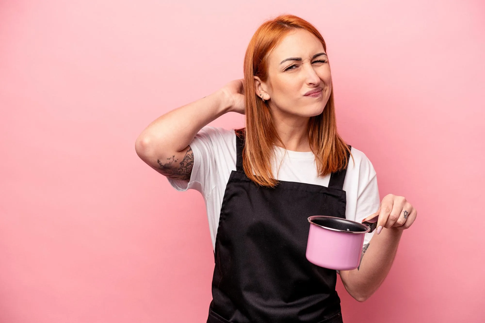 Young caucasian cooker woman holding translator isolated on pink background touching back of head, thinking and making a choice.