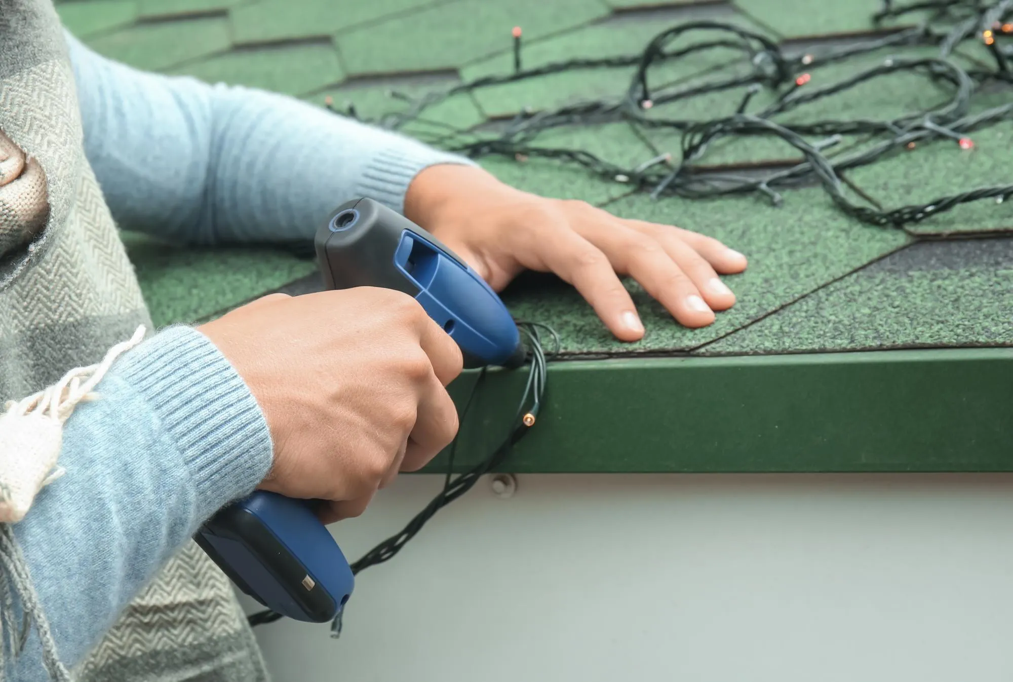 Young man hanging Christmas lights on roof of house