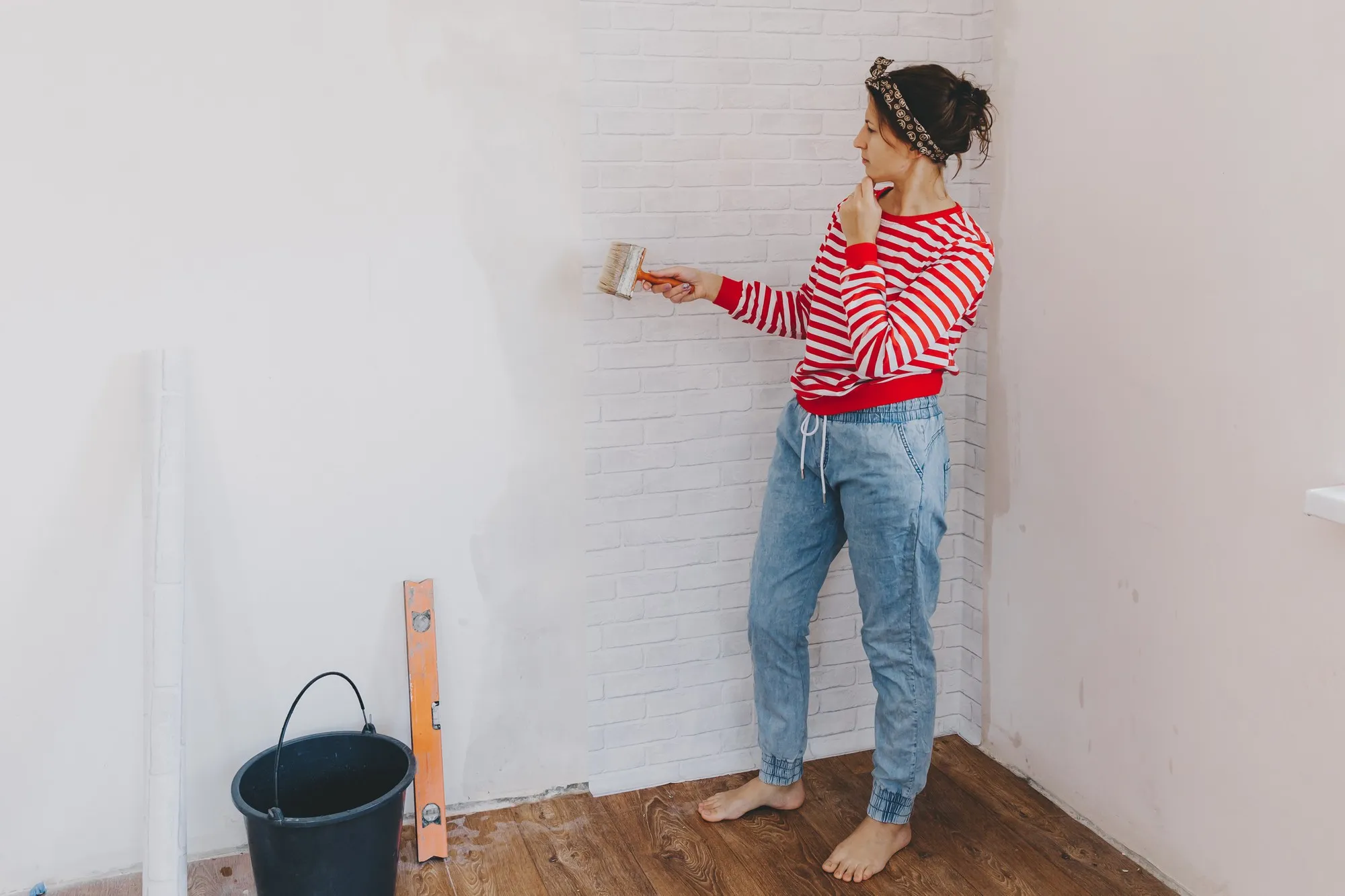 Young woman glues wallpaper at home. girl glues wallpaper in the form of a brick. repair.