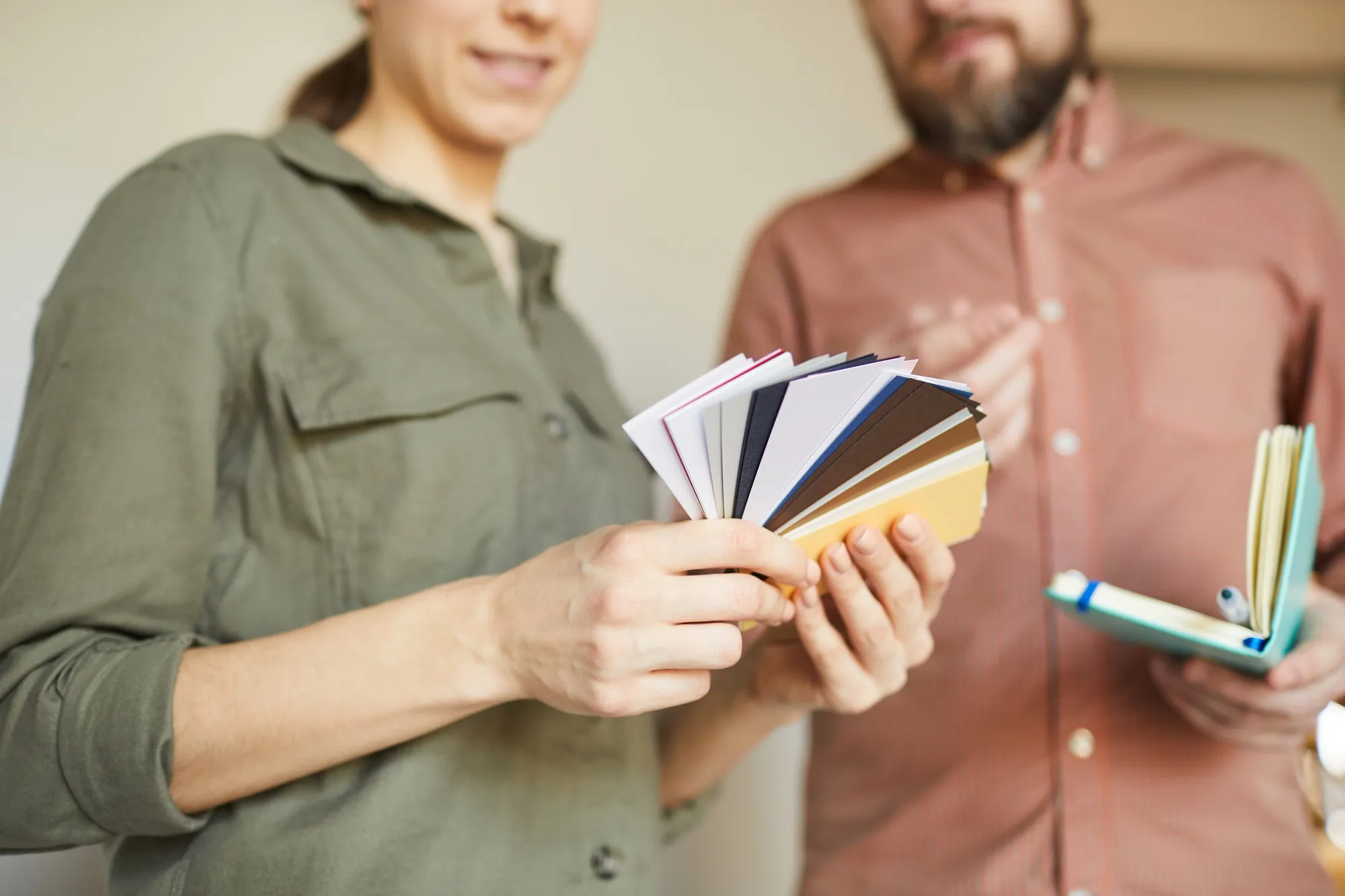 Close up of young couple looking at color samples standing by white blank wall while redecorating house, copy space