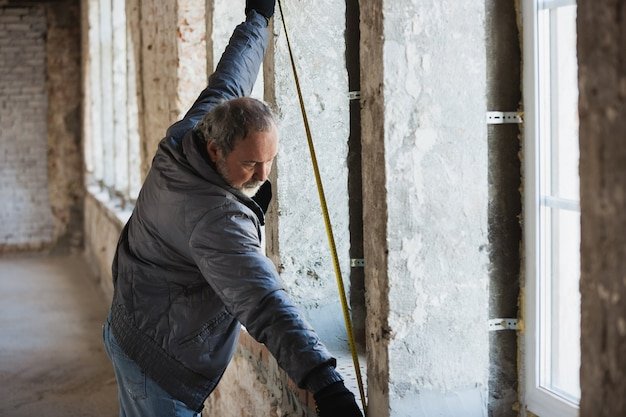 Closeup of repairman in uniform, professional builder working using construction equipment. Process of building, apartment renovation, repairing, building. Coloring, measuring, preparing the base.