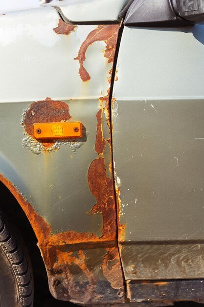 Closeup of a rusty car with a yellow light on its side