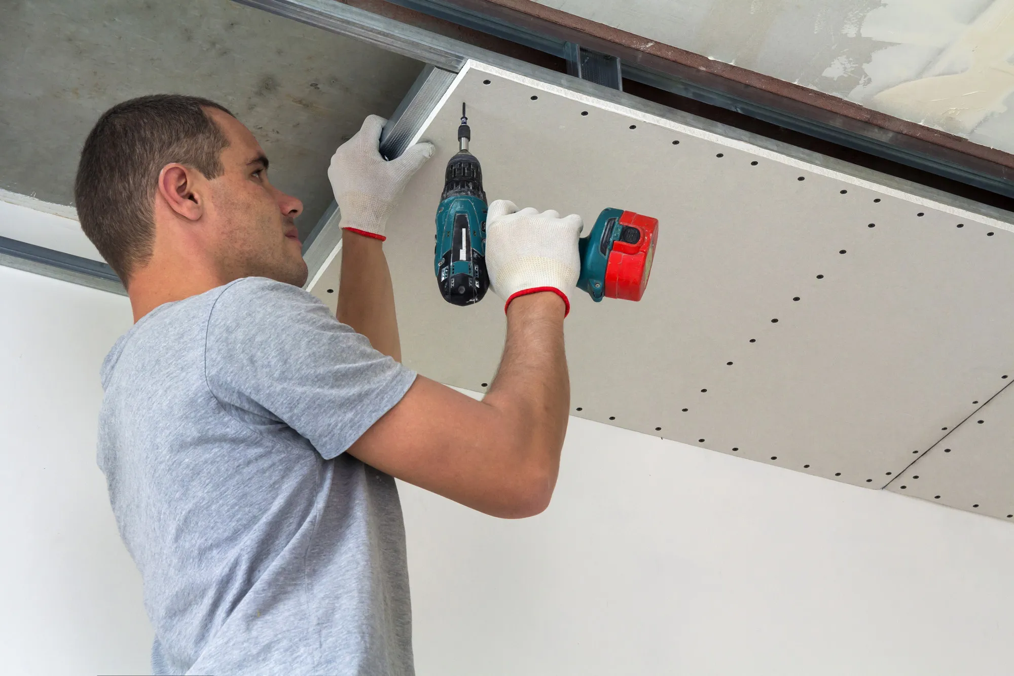 Construction worker assemble a suspended ceiling with drywall and fixing the drywall to the ceiling metal frame with screwdriver.