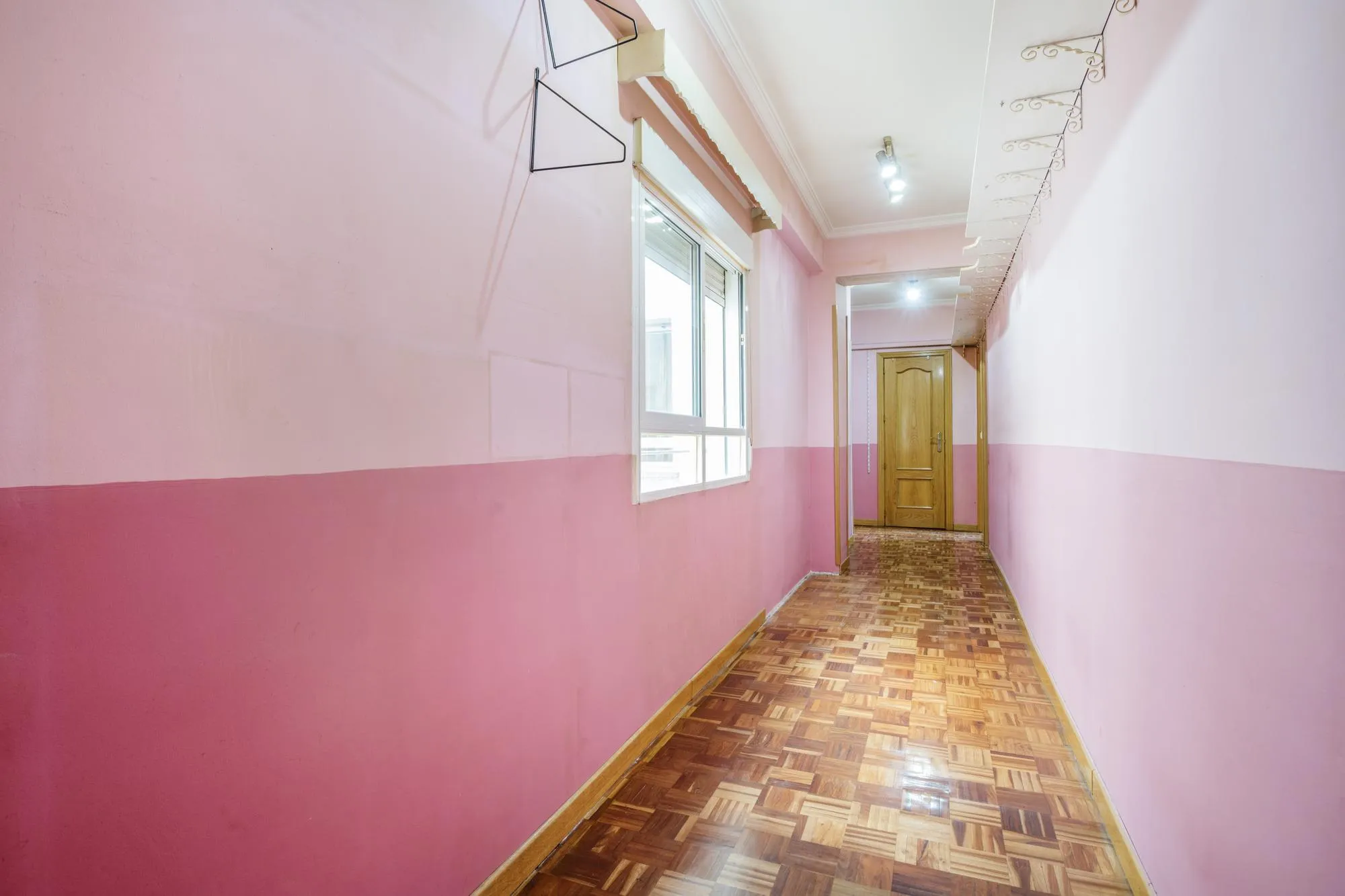 A corridor of an empty house with wooden parquet floors and windows with former owners with no taste for decoration