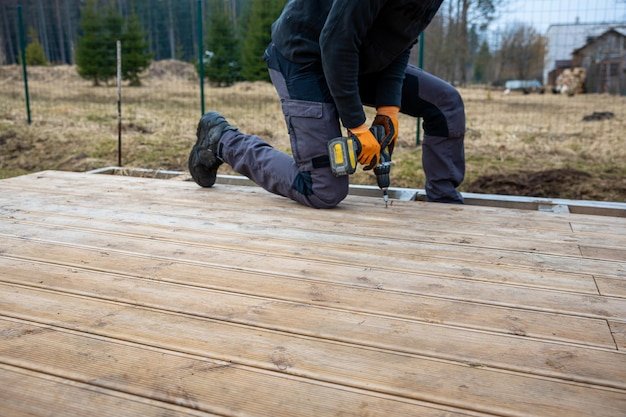 Deck or terrace construction builder hand with electric screwdriver installing impregnated wooden boards