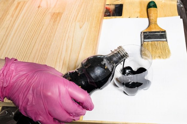 Gloved hand pours wood stain from bottle into jar