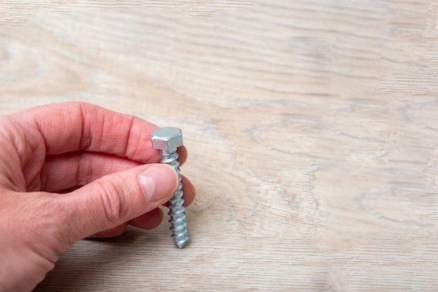 Hand holds a gray screw for screwing to a wooden background
