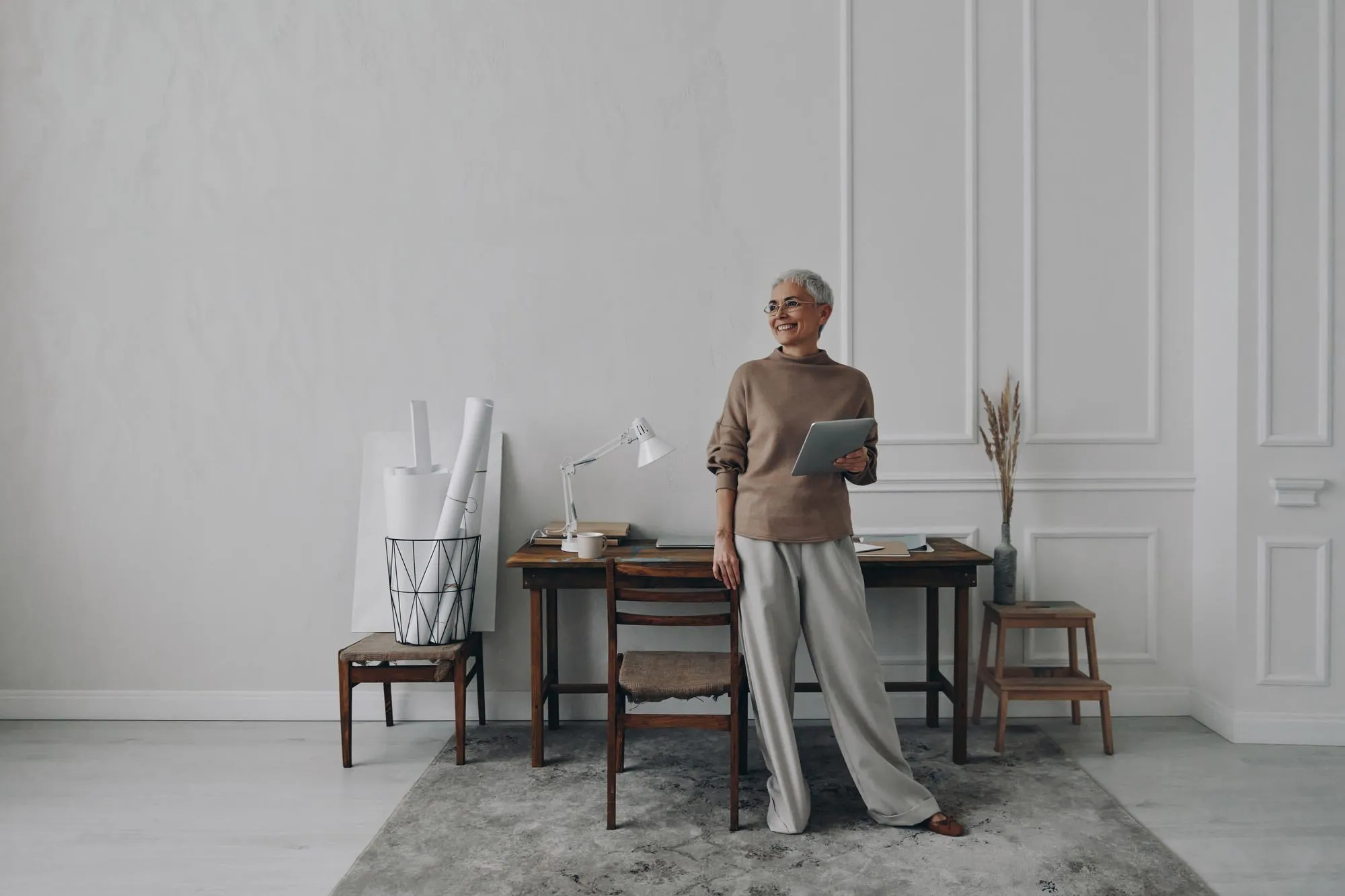 Happy senior woman holding digital tablet while standing near her working place