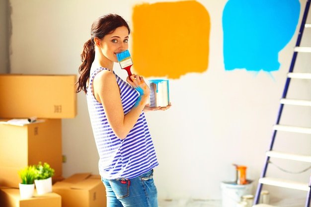 Happy smiling woman painting interior wall of new house