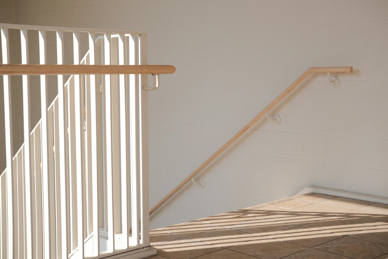 Sunlight streams through a white railing onto a wall.